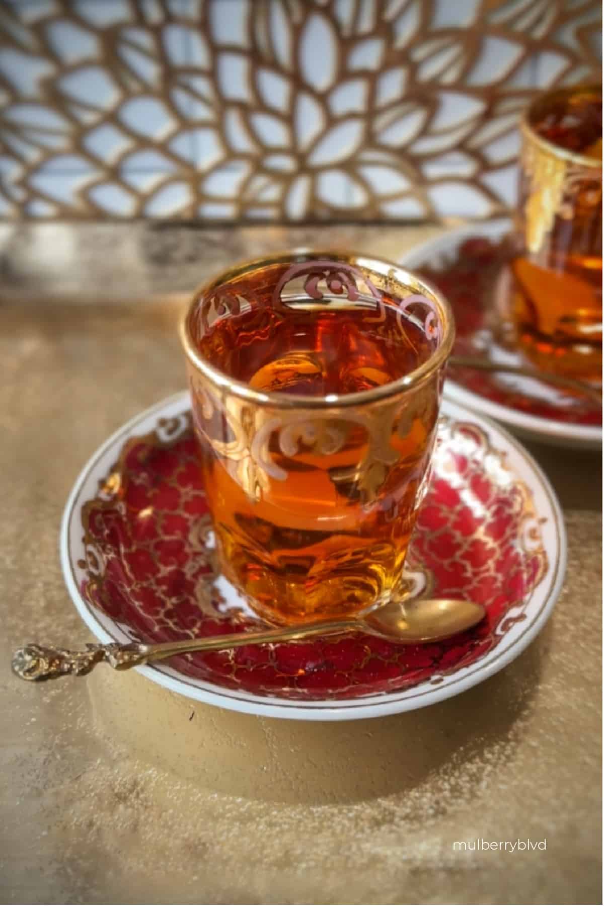 Glass of Persian black tea on saucer with spoon