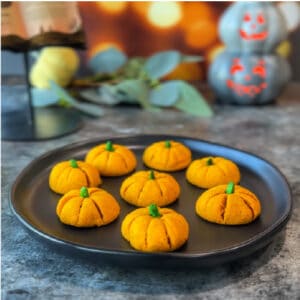 image of eight orange colored pumpkin shaped cookies on a black plate