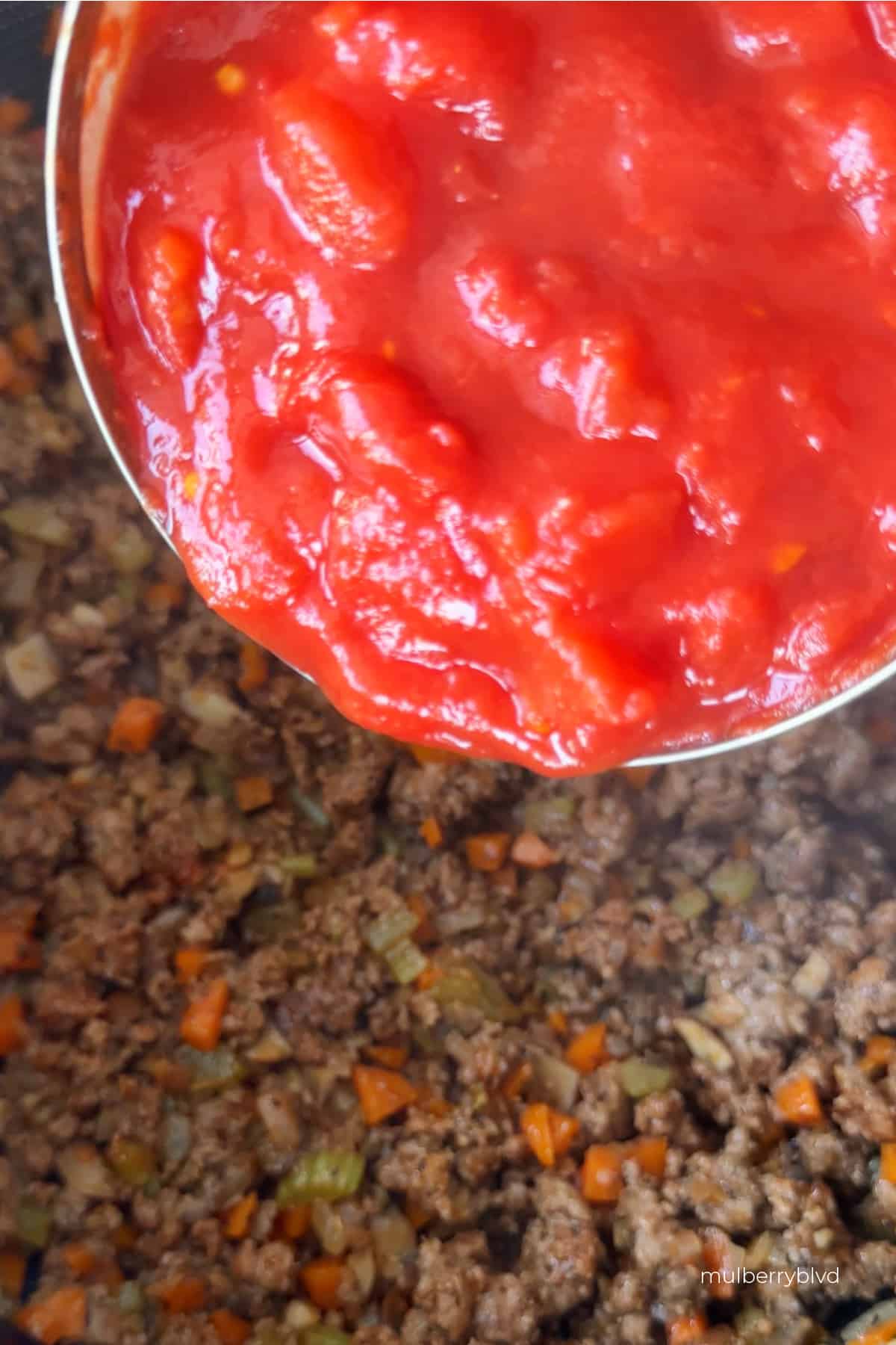 an image of a can of tomatoes being added to a mixture of cooked beef and finely chopped carrots, celery, mushrooms and onions