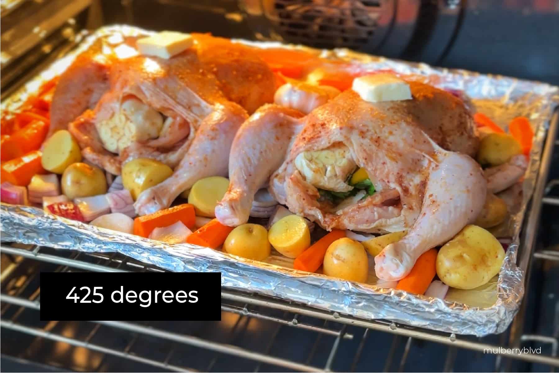 raw chicken, which is set on an aluminum foil lined baking tray, surrounded by raw potatoes, carrots, red onions, and garlic is being placed in an oven, with the text "425 degrees" written on the image