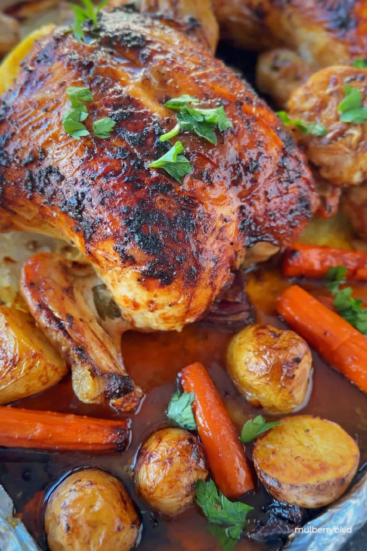 an image with a roasted chicken with parsley garnish on top, all on a sheet pan with roasted carrots, potatoes and garlic