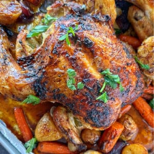 an image with a roasted chicken with parsley garnish on a sheet pan with roasted carrots, potatoes and garlic