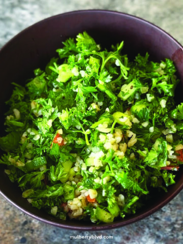 A bowl of tabouli (tabbouleh) made with lots of parsley, mint, tomatoes, cucumbers, bulgur and a lemon and olive oil dressing